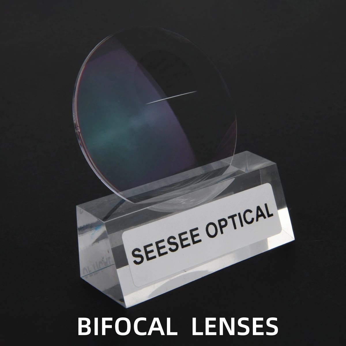 A bifocal lens standing in a clear acrylic block engraved Seesee Optical, segment line visible, dark background