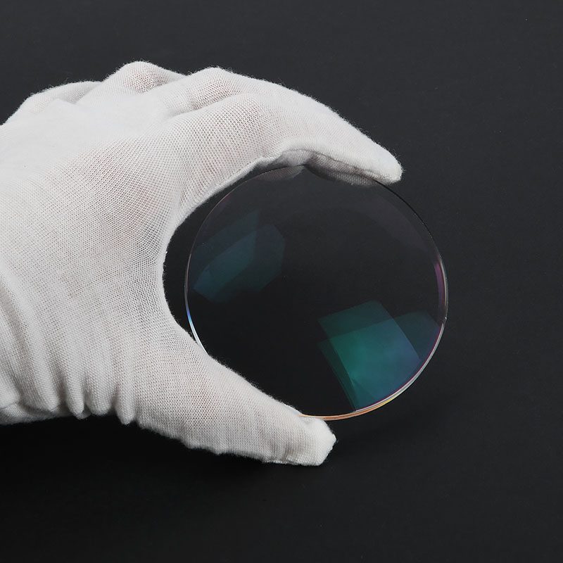 A clear base blue cut lens held in a white glove, blue and green residual reflections