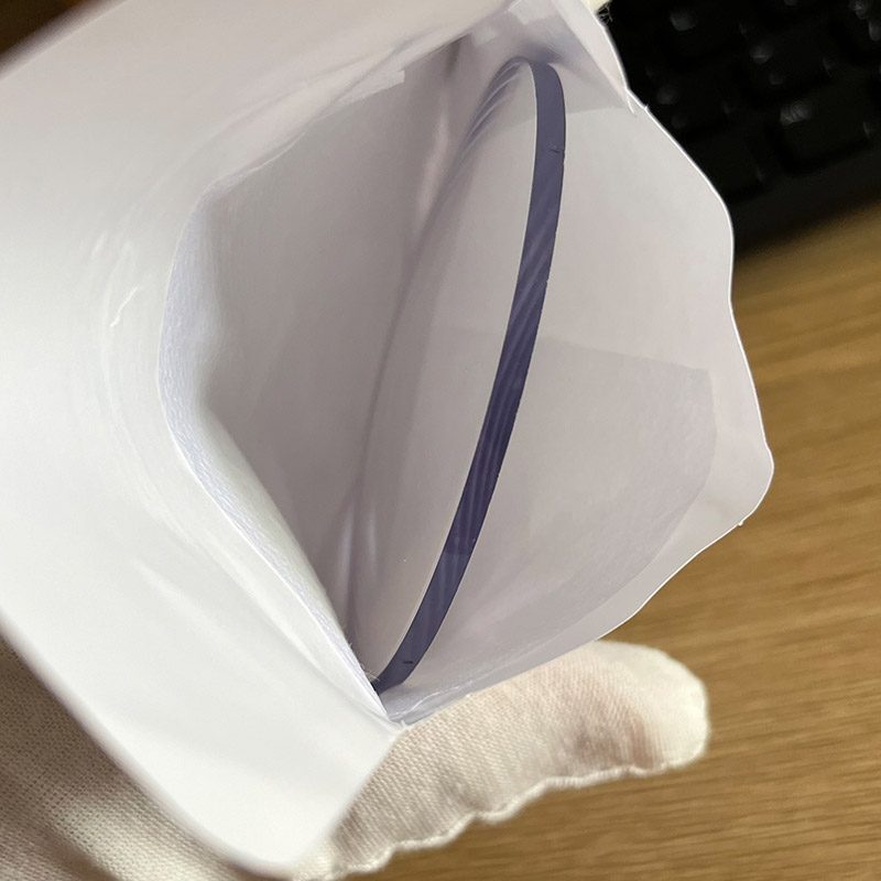A finished lens half out of its white protective envelope, held in a white glove