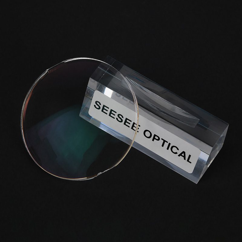 A polycarbonate lens with hard multi coating standing in a clear acrylic block engraved Seesee Optical, dark background