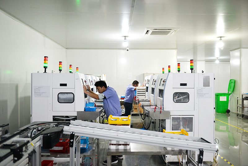 A technician at an enclosed production line with signal towers in a white clean room