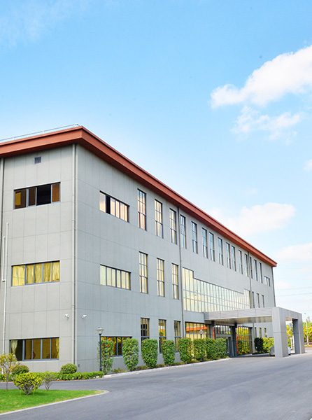 A three-storey white factory building with a covered entrance and a hedge