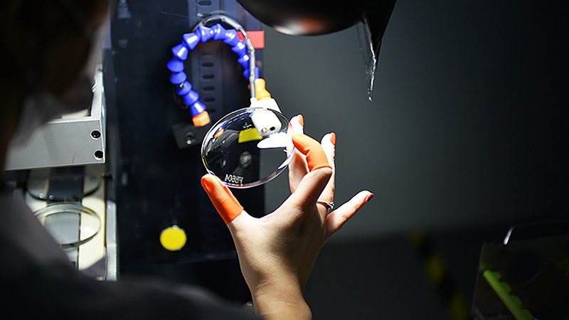 A hand holding a lens under a blue ring lamp for inspection