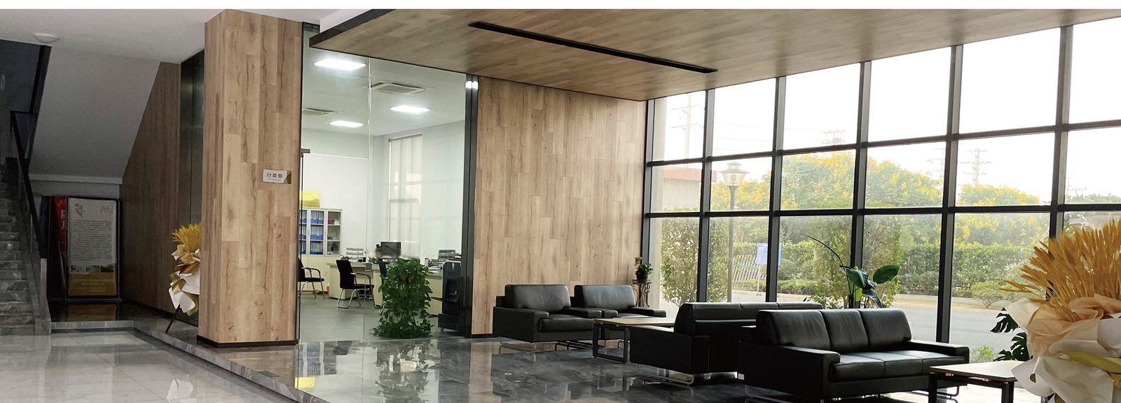 A reception lobby with wood panelling, black sofas and a wall of windows