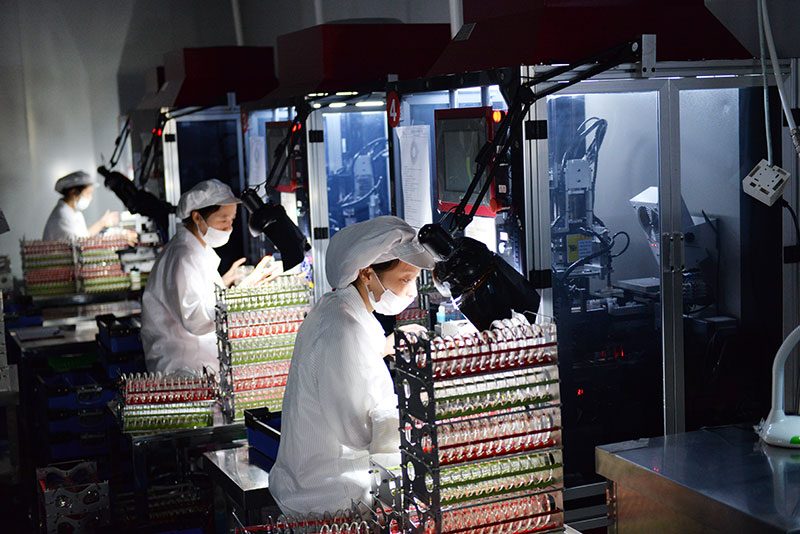 Workers in white coats fitting glass moulds with coloured gaskets on a bench at the Seesee plant