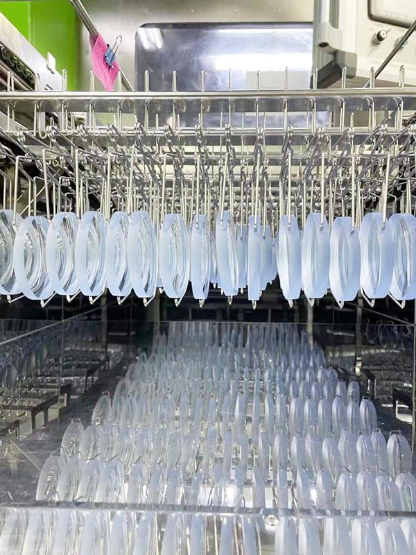 Rows of cast lenses hanging in racks along a cleaning line