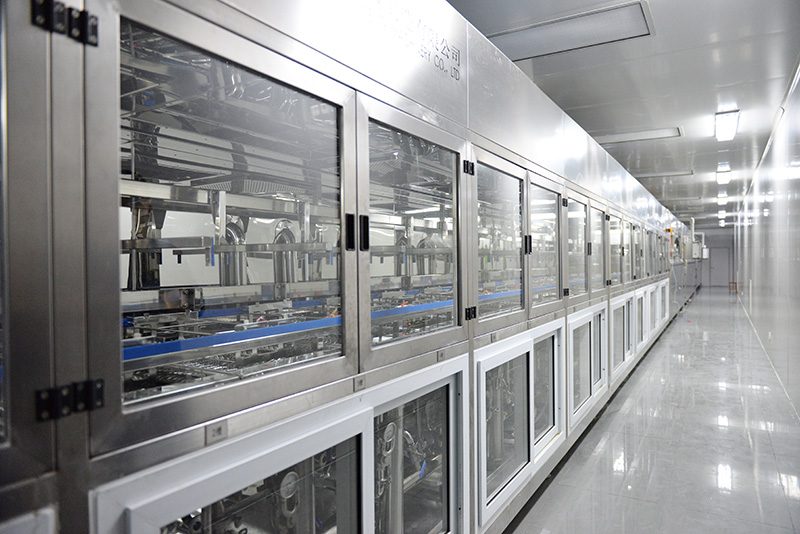An enclosed hard-coating line in a white room, lenses moving through glass cabinets