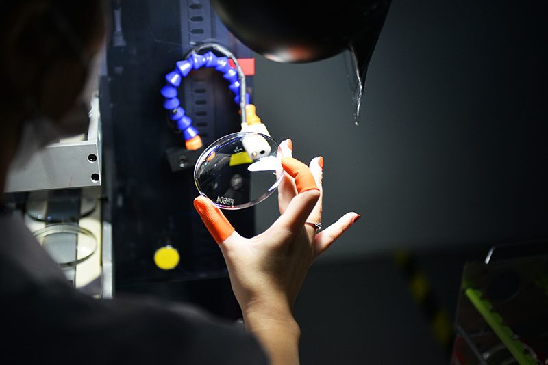 An inspector holding a lens up to a lamp for visual inspection